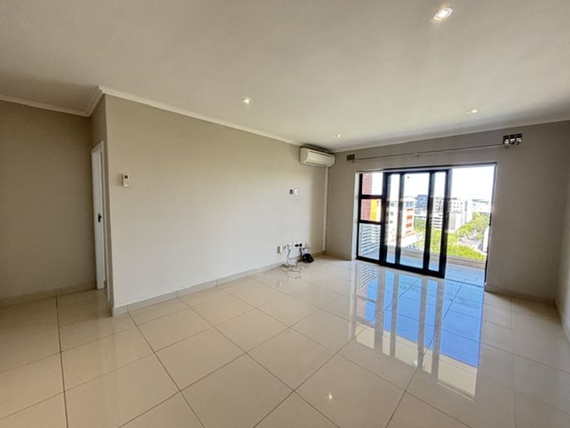 Spacious, light-filled living area featuring polished tile flooring, recessed lighting, and a large sliding glass door providing access to the balcony.