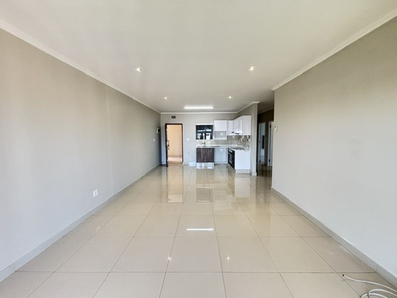 Spacious open-plan living area featuring polished tile flooring, recessed lighting, and a modern kitchen with built-in cabinetry and appliances.