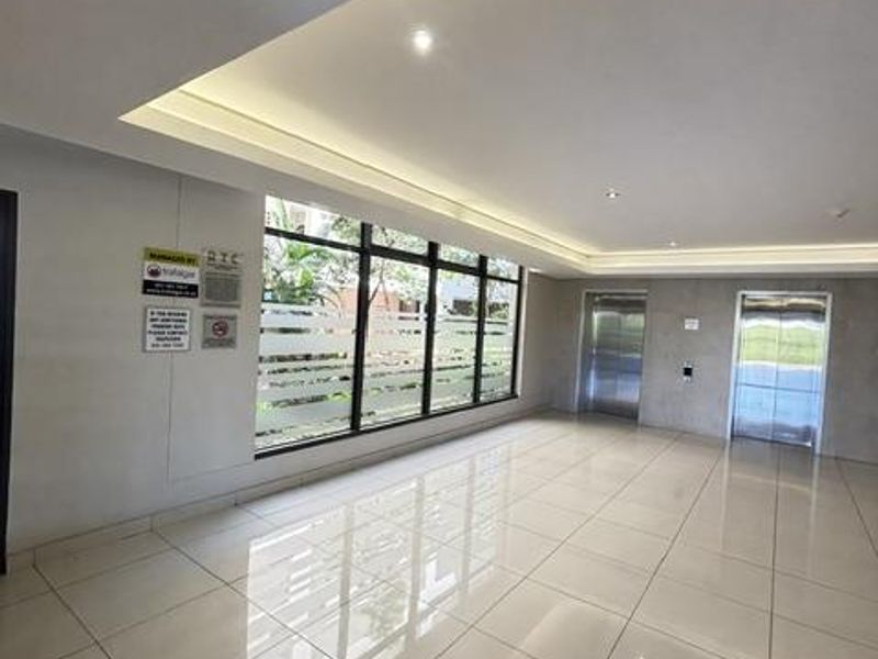 A modern, spacious apartment building lobby featuring polished large-format floor tiles, recessed cove lighting, and elevator access.