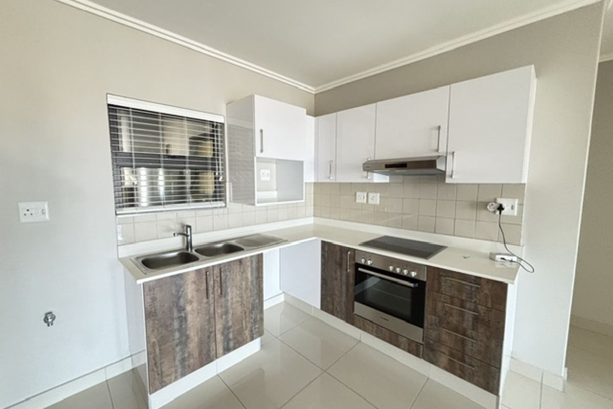 Modern kitchen featuring two-tone cabinetry, stainless steel appliances including a built-in oven and hob, tiled backsplash, and neutral floor tiles.