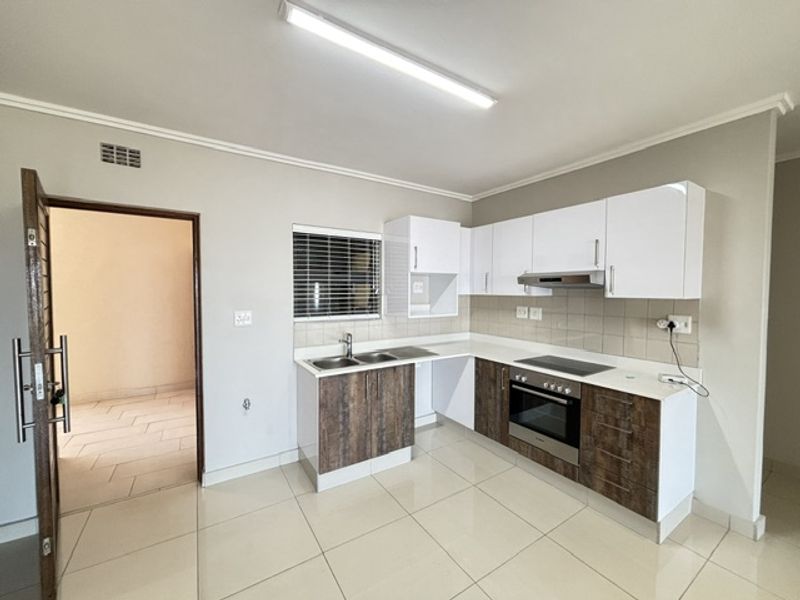 Modern kitchen featuring two-tone cabinetry, integrated oven and hob, tiled backsplash, and neutral floor tiles in an open-plan layout.