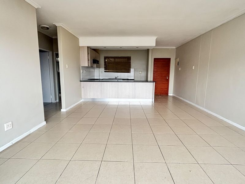 Spacious open-plan living area featuring neutral tiled flooring and a functional kitchen with built-in cabinetry and a breakfast counter.