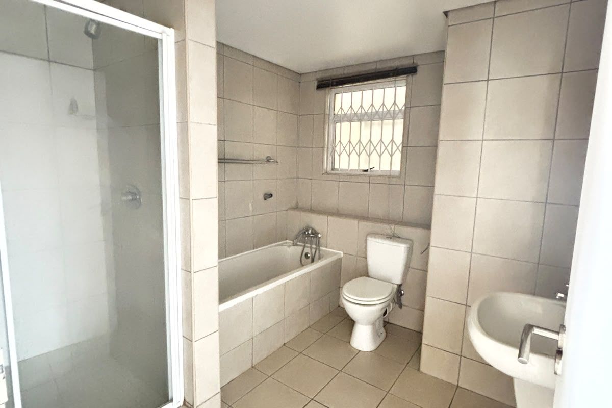 A functional bathroom featuring a separate shower enclosure, built-in bathtub, pedestal basin, and toilet, finished with neutral floor-to-ceiling wall tiles.
