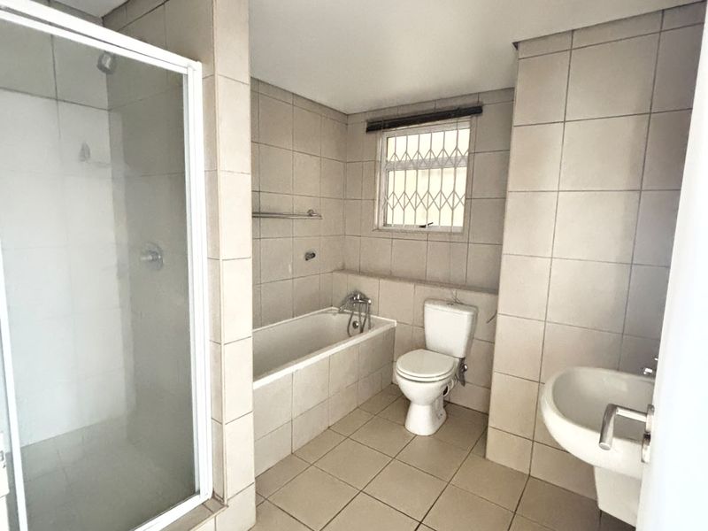 A functional bathroom featuring a separate shower enclosure, built-in bathtub, pedestal basin, and toilet, finished with neutral floor-to-ceiling wall tiles.
