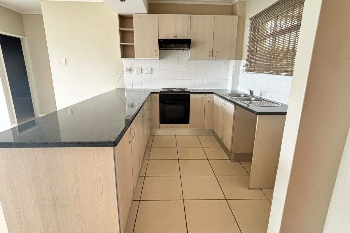 A functional kitchen featuring light wood cabinetry, granite countertops, a built-in oven with extractor fan, and tiled flooring throughout.