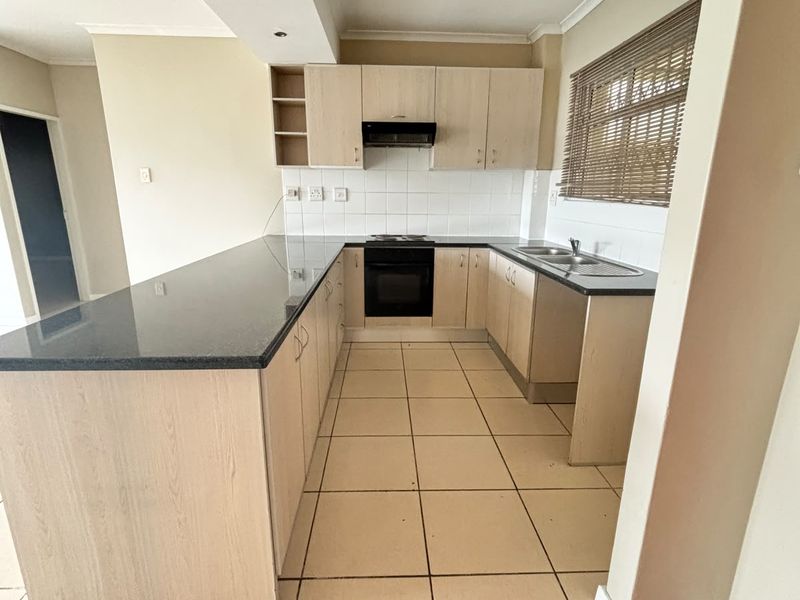 A functional kitchen featuring light wood cabinetry, granite countertops, a built-in oven with extractor fan, and tiled flooring throughout.