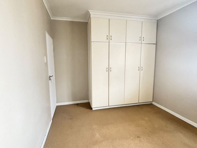 An empty bedroom featuring built-in cupboards, neutral wall finishes, and carpeted flooring in need of replacement.