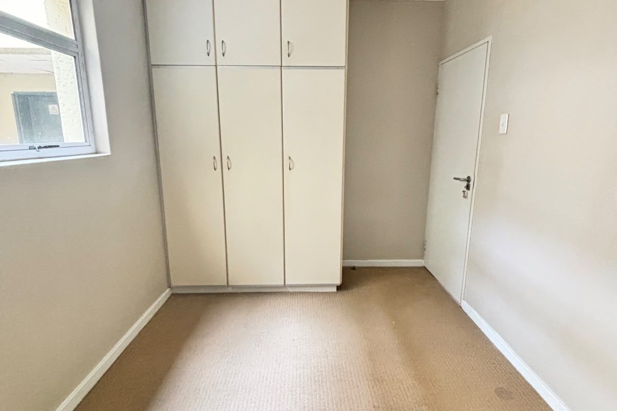 An empty bedroom featuring built-in cupboards, neutral wall finishes, and carpeted flooring, offering a blank canvas for personalization.