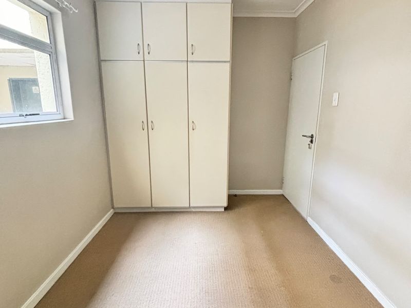 An empty bedroom featuring built-in cupboards, neutral wall finishes, and carpeted flooring, offering a blank canvas for personalization.