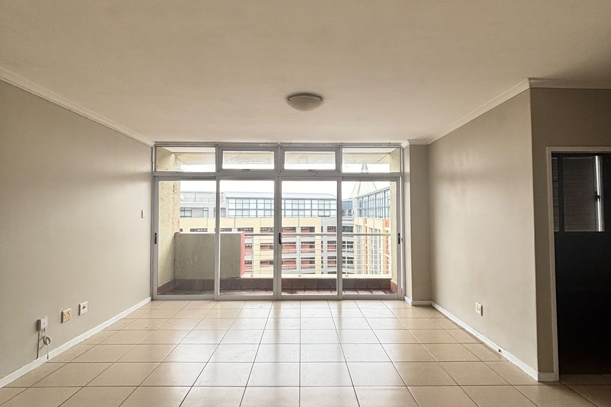 A spacious, empty living area featuring neutral tiled flooring and a large sliding glass door that opens onto a balcony.