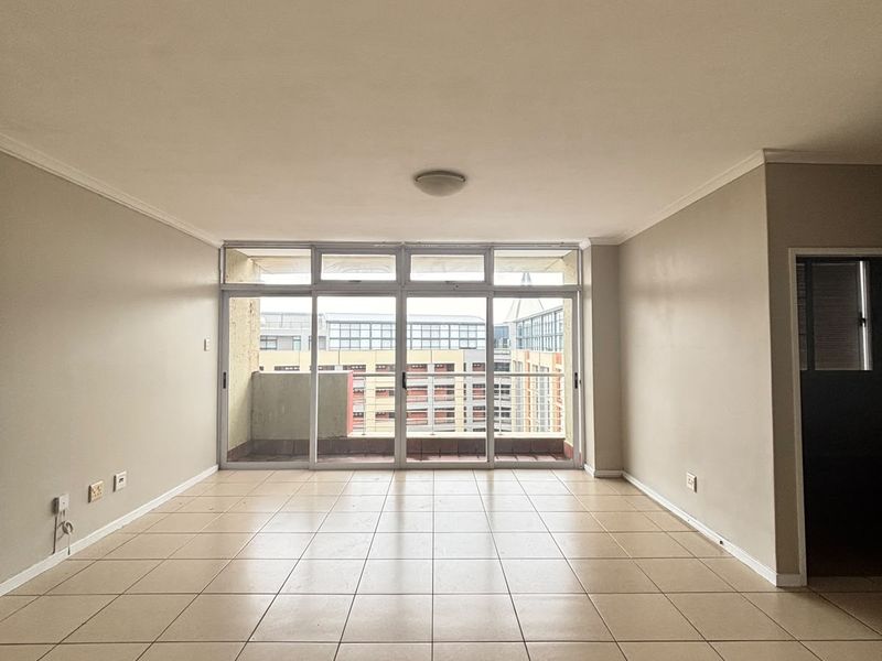A spacious, empty living area featuring neutral tiled flooring and a large sliding glass door that opens onto a balcony.