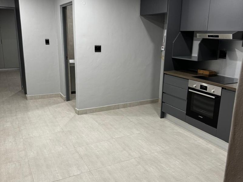 Modern kitchen featuring sleek dark grey cabinetry, integrated oven and hob, recessed lighting, and neutral tiled flooring in an open-plan layout.