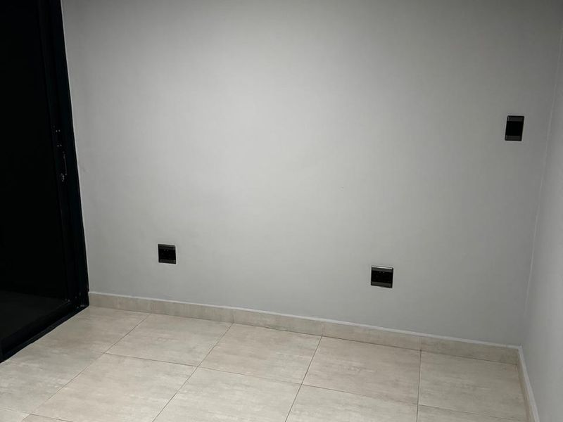 A clean, empty living space featuring neutral tiled flooring, modern electrical outlets, and a dark-framed sliding glass door leading to an exterior area.