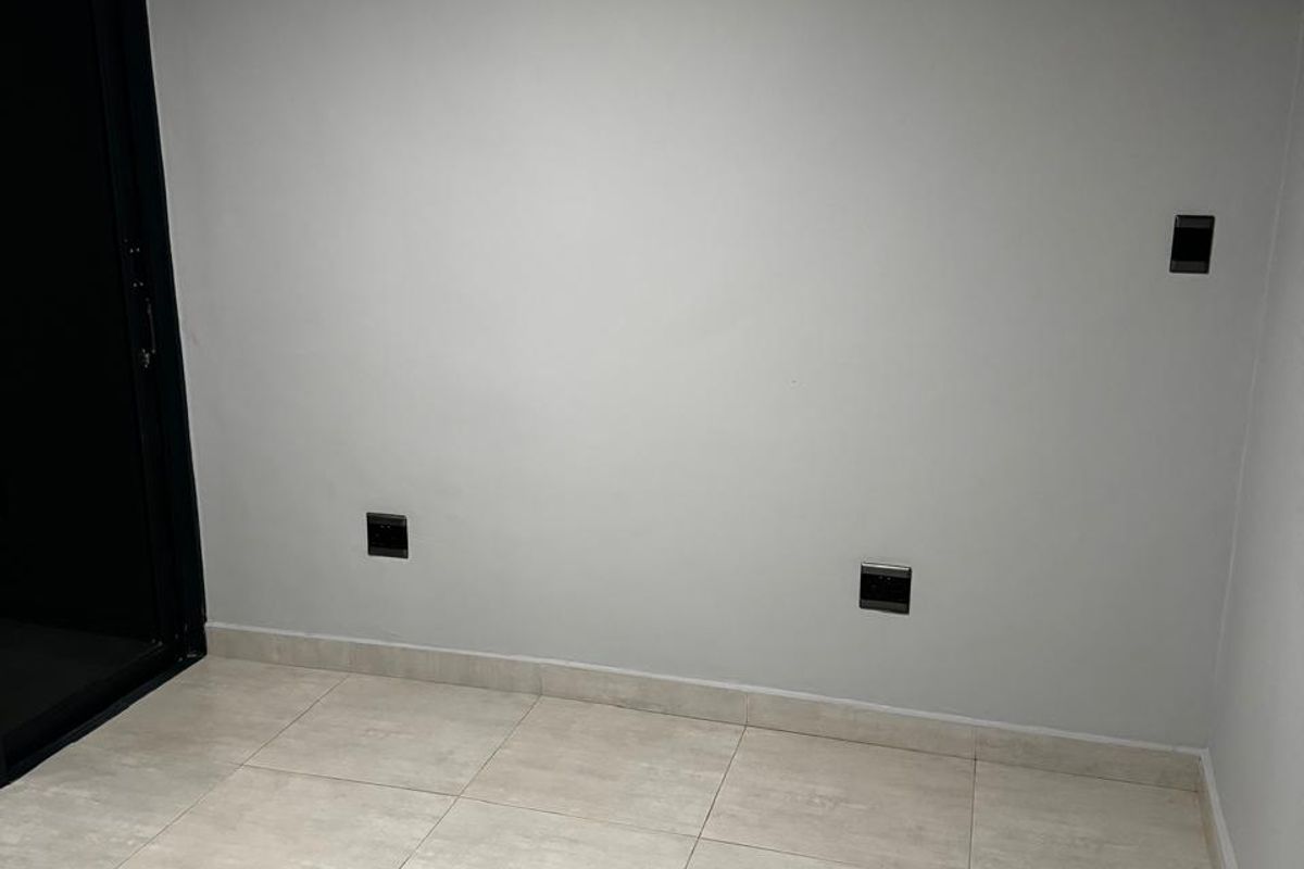 A clean, empty living space featuring neutral tiled flooring, modern electrical outlets, and a dark-framed sliding glass door leading to an exterior area.