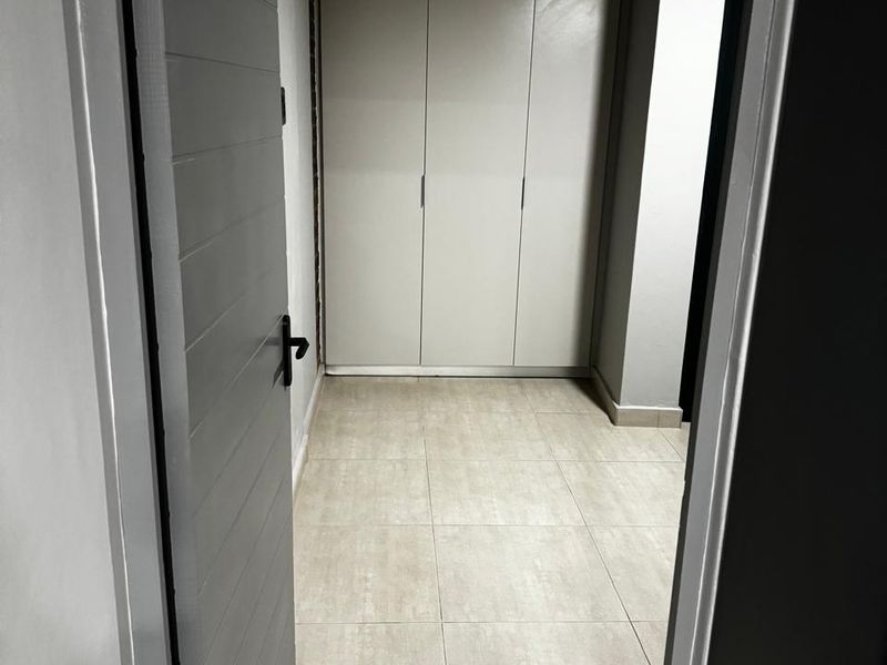 A clean, empty bedroom featuring neutral tiled flooring and modern built-in cupboards, viewed through an open doorway.