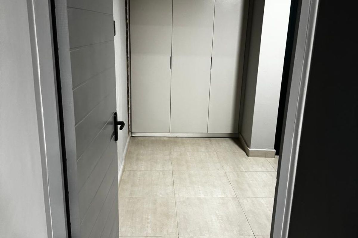 A clean, empty bedroom featuring neutral tiled flooring and modern built-in cupboards, viewed through an open doorway.