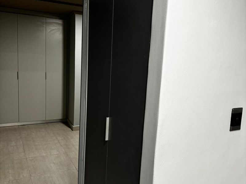 A clean hallway featuring neutral tiled flooring and modern built-in cupboards with dark finishes.
