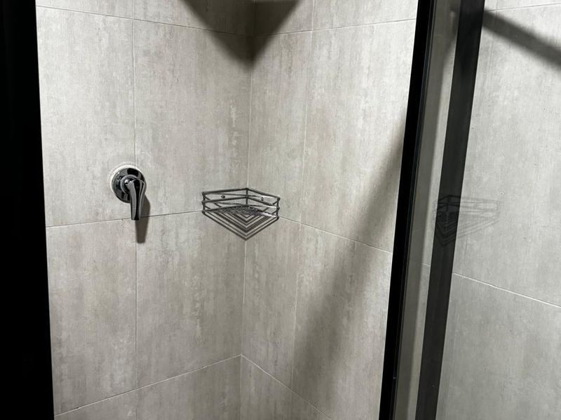 A modern, clean shower stall featuring large-format grey wall tiles, a rainfall shower head, and a sleek black-framed glass enclosure.