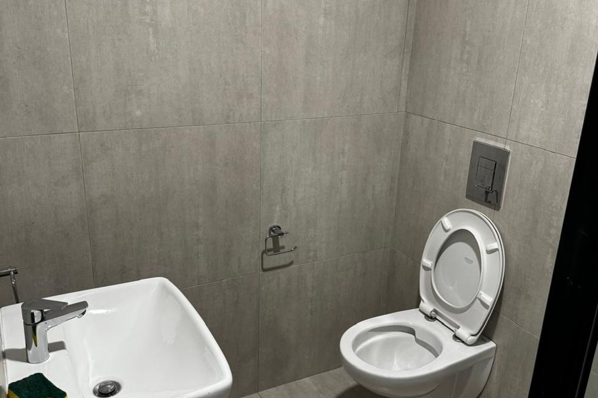 A modern, compact bathroom featuring grey tiled walls and flooring, a wall-mounted toilet with a concealed cistern, and a sleek vanity basin.
