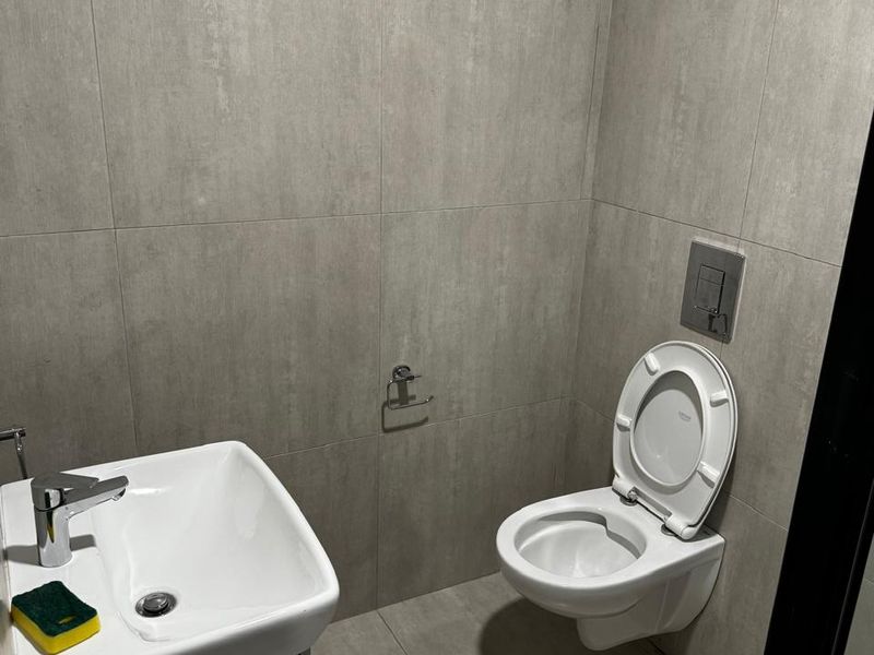 A modern, compact bathroom featuring grey tiled walls and flooring, a wall-mounted toilet with a concealed cistern, and a sleek vanity basin.
