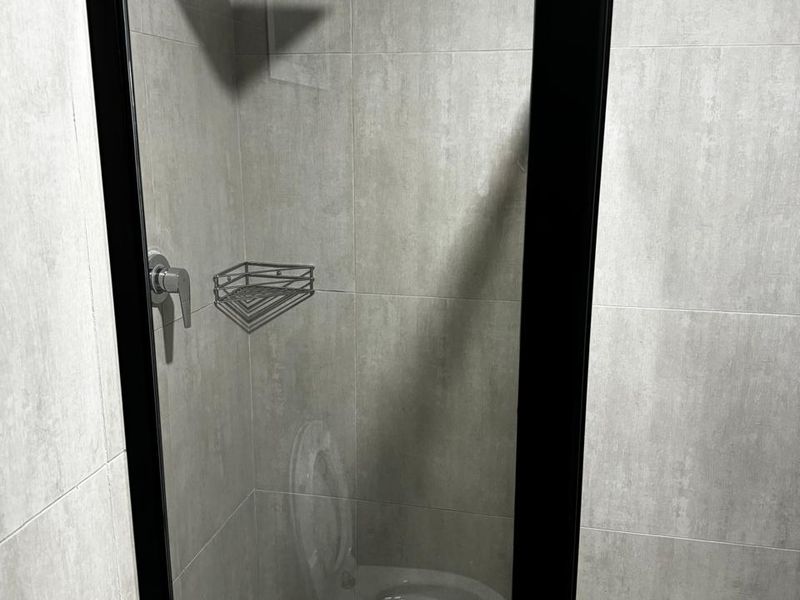 A modern bathroom shower enclosure featuring grey wall tiles, a black-framed glass door, and a contemporary rain shower head.
