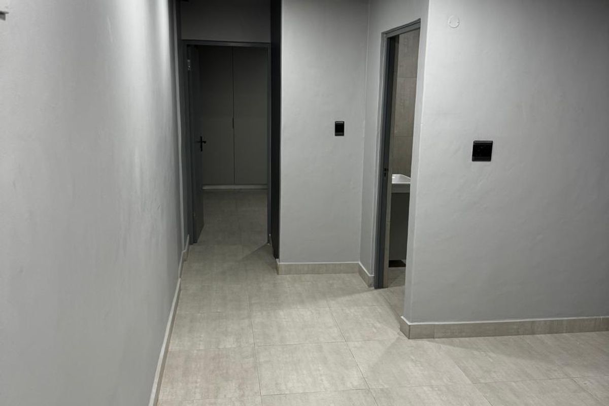 A clean, empty hallway featuring neutral grey walls, modern tiled flooring, and recessed ceiling lighting, providing access to adjacent rooms.