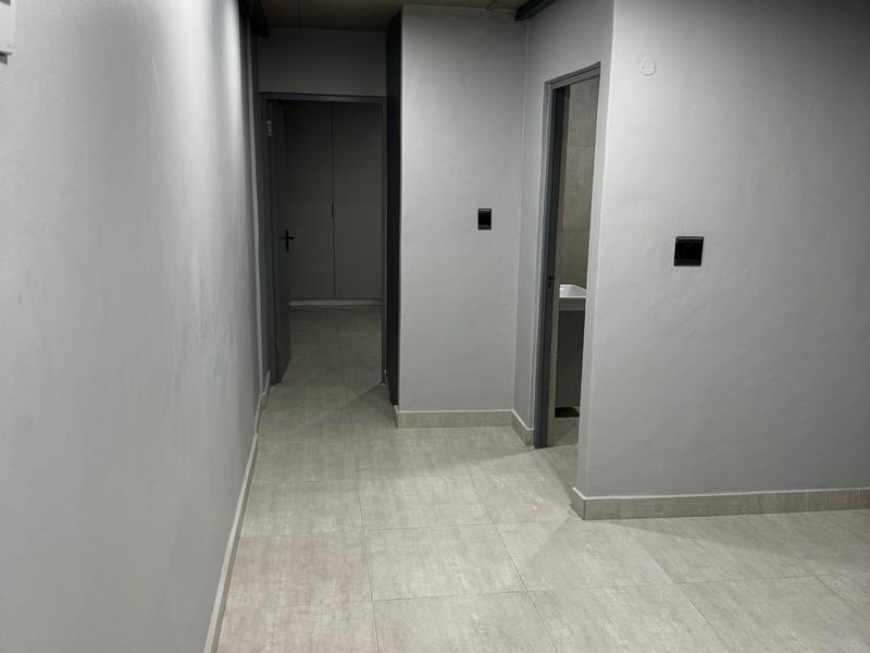 A clean, empty hallway featuring neutral grey walls, modern tiled flooring, and recessed ceiling lighting, providing access to adjacent rooms.