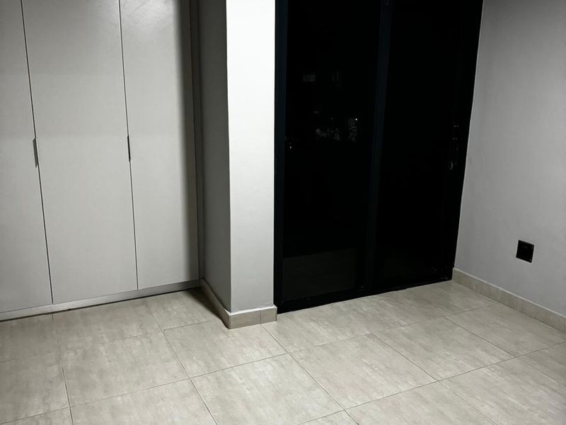 A clean, empty bedroom featuring neutral tiled flooring, a modern built-in wardrobe, and a sliding glass door providing access to the exterior.