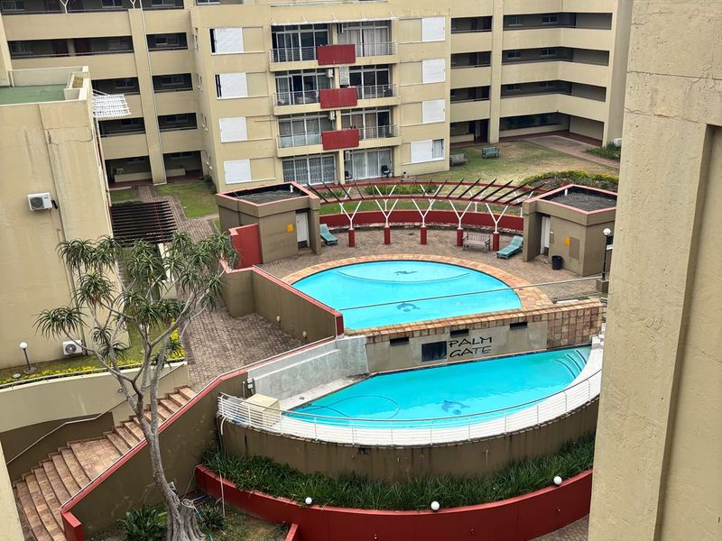 Elevated view of the apartment complex communal pool area featuring tiered swimming pools, paved courtyard, and landscaped garden beds.