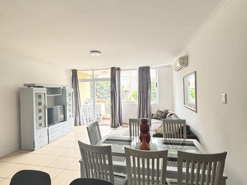 Open-plan living and dining area featuring tiled flooring, a wall-mounted air conditioner, and direct access to a balcony through sliding glass doors.