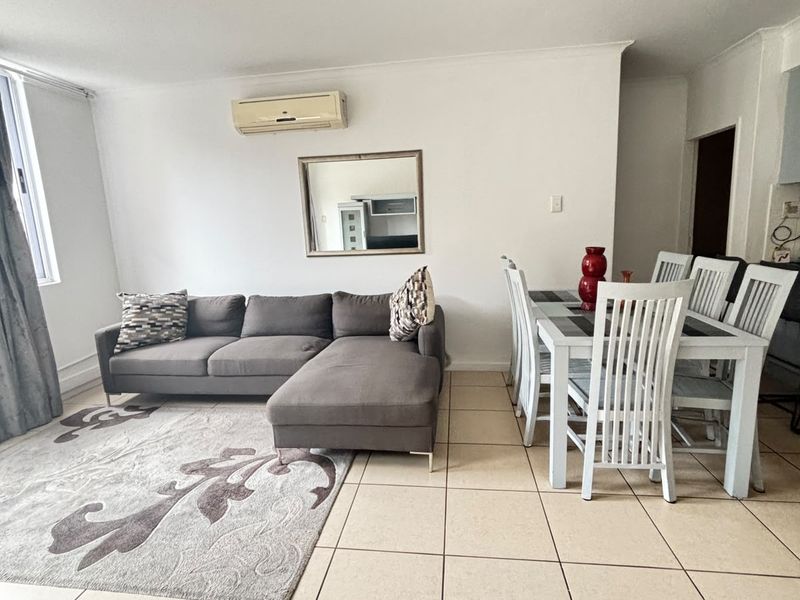 Open-plan living and dining area featuring neutral ceramic floor tiles and a wall-mounted split-system air conditioner.
