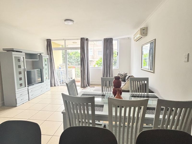 Spacious open-plan living and dining area featuring tiled flooring, a wall-mounted air conditioner, and direct access to a balcony through sliding glass doors.