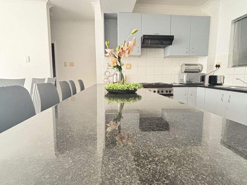 Open plan kitchen featuring a large granite breakfast bar, built-in cabinetry, and integrated appliances, creating a functional and modern living space.
