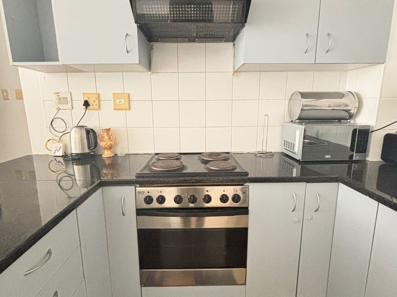 A compact kitchen featuring light-colored cabinetry, granite countertops, a built-in oven with an electric hob, and a tiled backsplash.