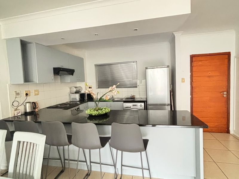 Open plan kitchen featuring a granite breakfast bar, built-in cabinetry, and tiled flooring, seamlessly integrated with the living area.