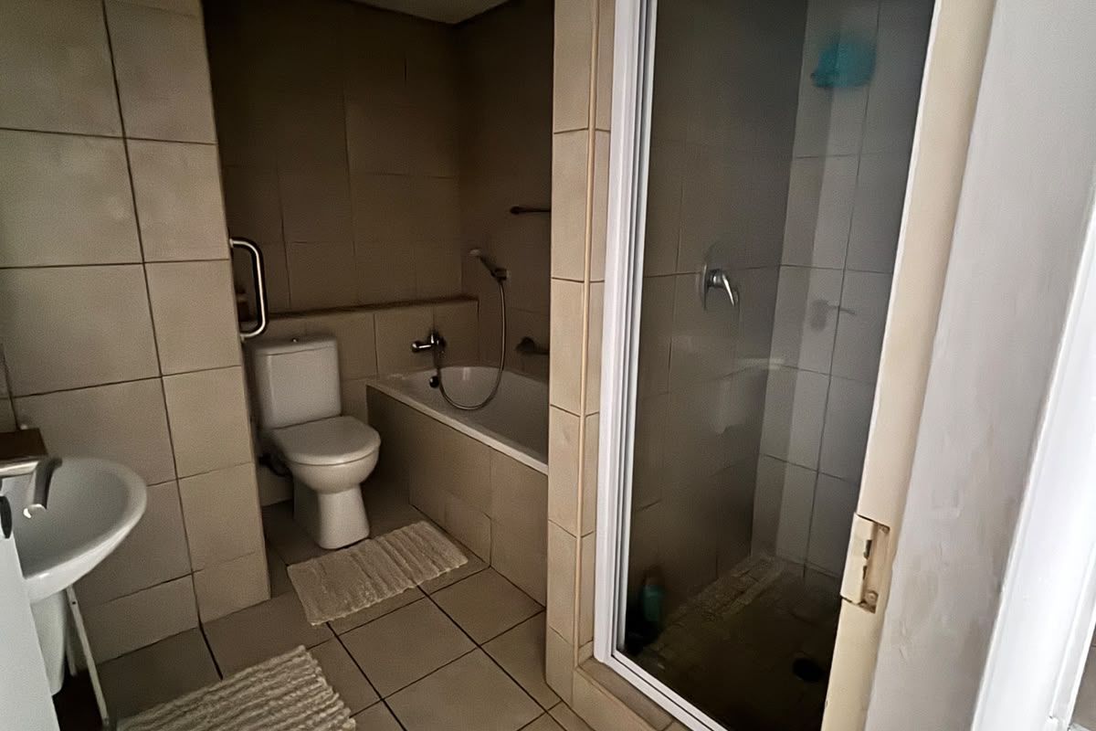 A functional bathroom featuring a separate shower enclosure, bathtub, toilet, and pedestal basin with neutral wall and floor tiling.