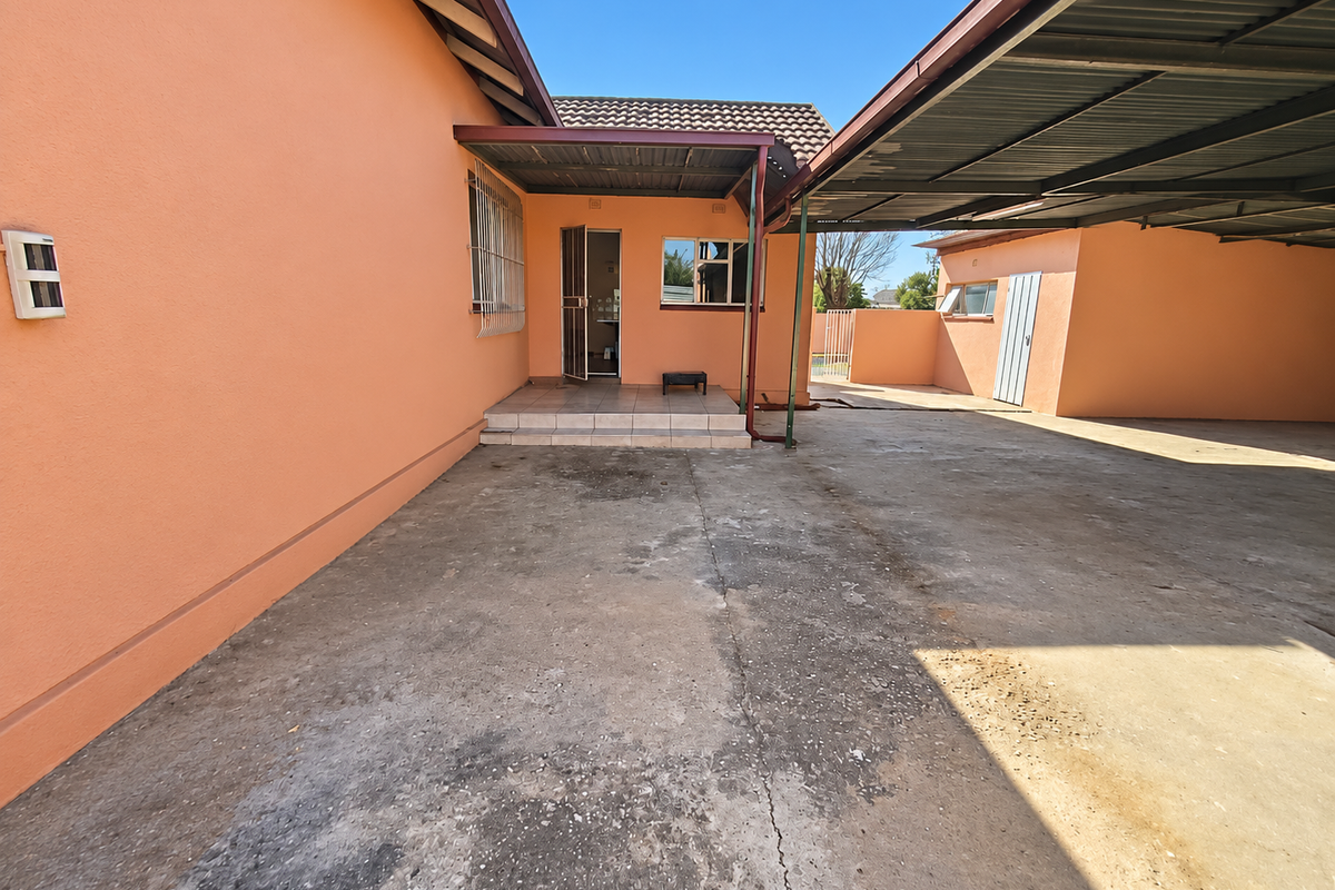 Rear exterior view featuring a concrete driveway, covered carport area, and tiled entrance steps leading to the main dwelling.