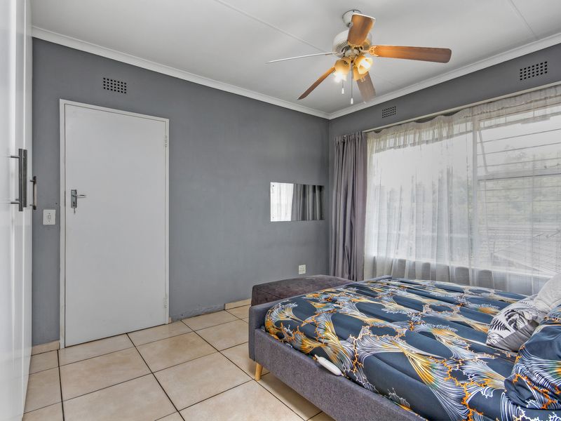 A bedroom featuring tiled flooring, a ceiling fan, and built-in cupboards, offering a functional and neutral living space.