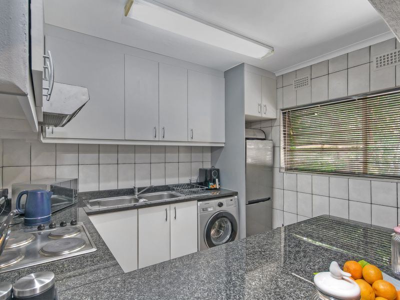 Functional kitchen featuring granite countertops, ample cabinetry, built-in electric hob, extractor fan, and integrated laundry plumbing for added convenience.