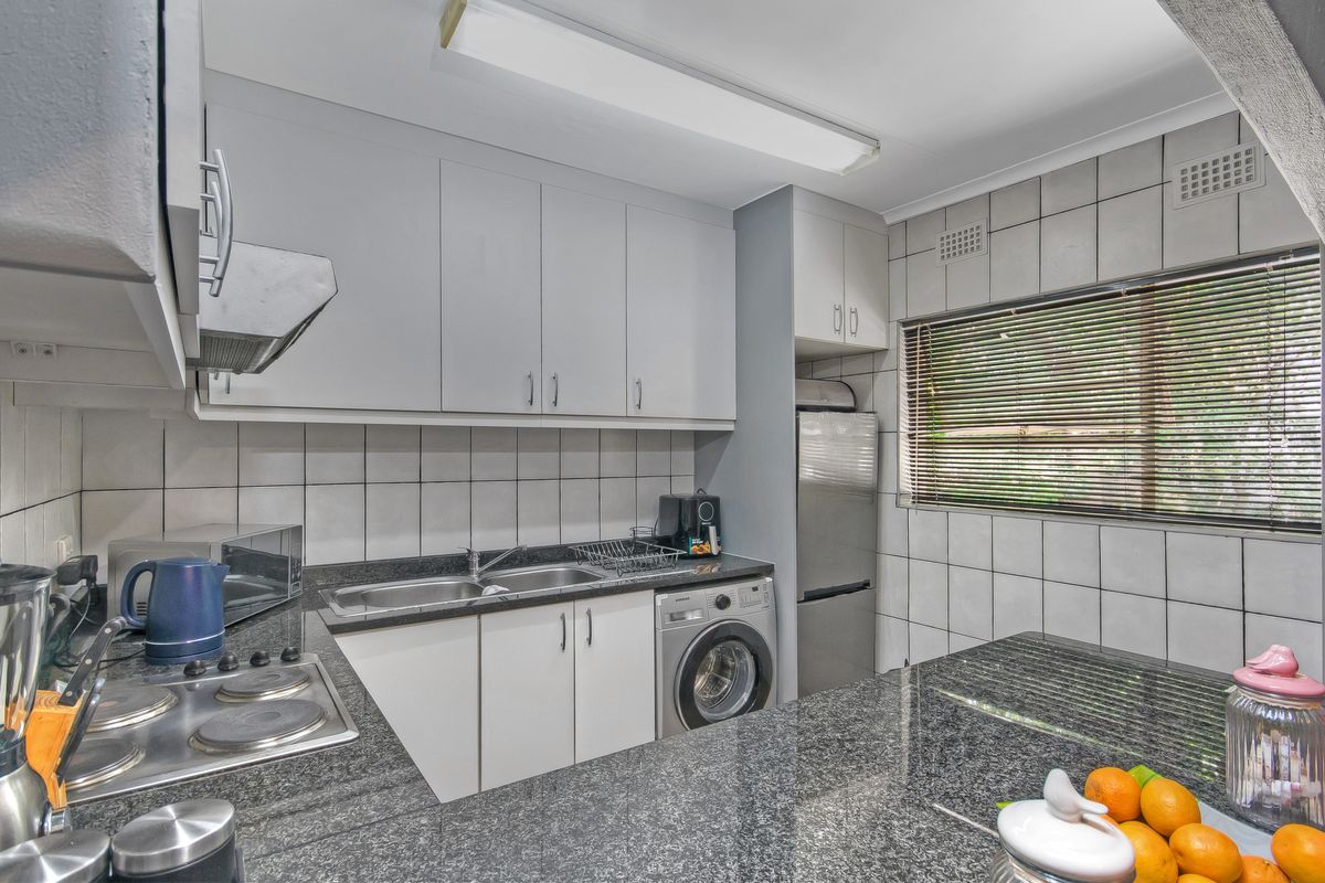 Functional kitchen featuring granite countertops, ample cabinetry, built-in electric hob, extractor fan, and integrated laundry plumbing for added convenience.