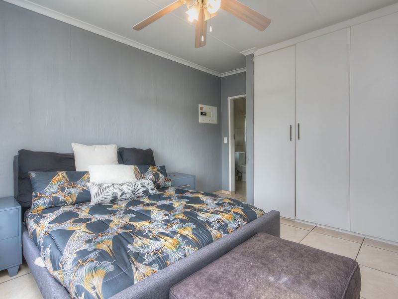 A well-maintained bedroom featuring built-in cupboards, tiled flooring, and a ceiling fan, with an adjoining en-suite bathroom visible.