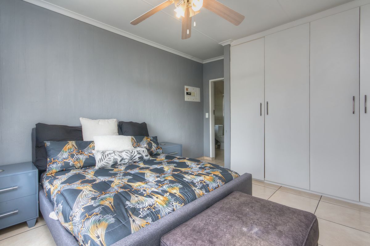 A well-maintained bedroom featuring built-in cupboards, tiled flooring, and a ceiling fan, with an adjoining en-suite bathroom visible.