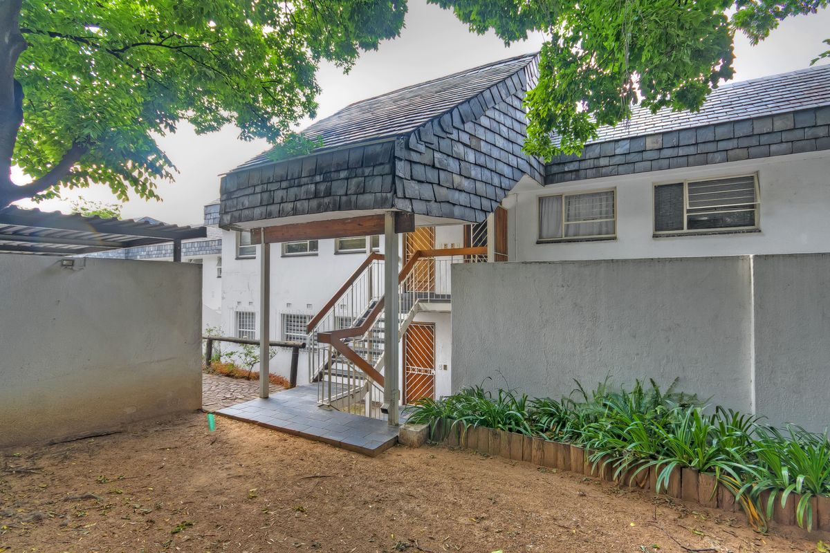 Rear exterior view of the townhouse featuring a unique slate-tiled roof, external staircase access, and a private courtyard area with established garden beds.