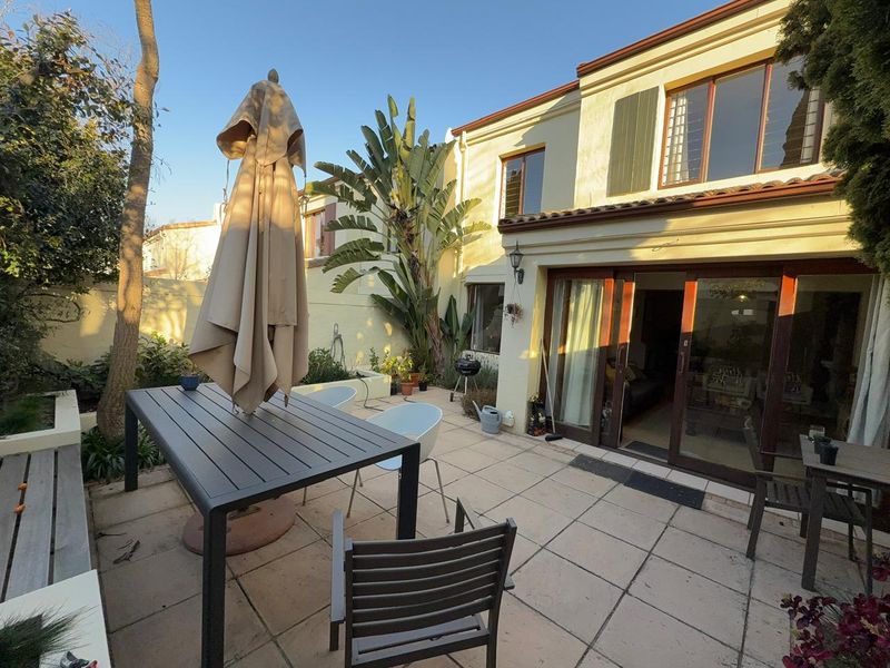 Rear exterior view of the townhouse featuring a paved patio area, raised garden beds, and sliding glass doors leading into the living space.