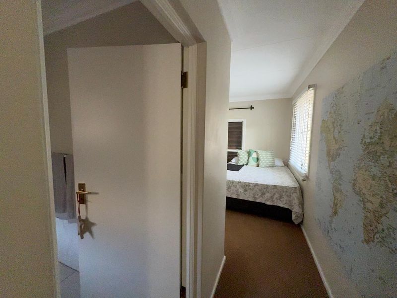 A view from a hallway into a bedroom featuring neutral walls, carpeted flooring, and venetian blinds.
