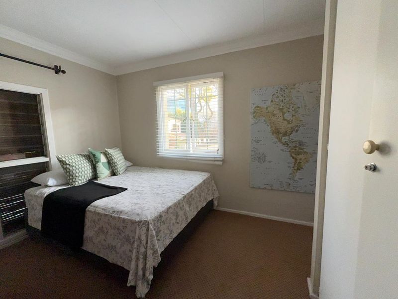 A standard bedroom featuring carpeted flooring, neutral wall tones, and venetian blinds on the window.