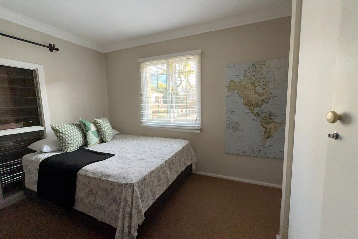 A standard bedroom featuring carpeted flooring, neutral wall tones, and venetian blinds on the window.