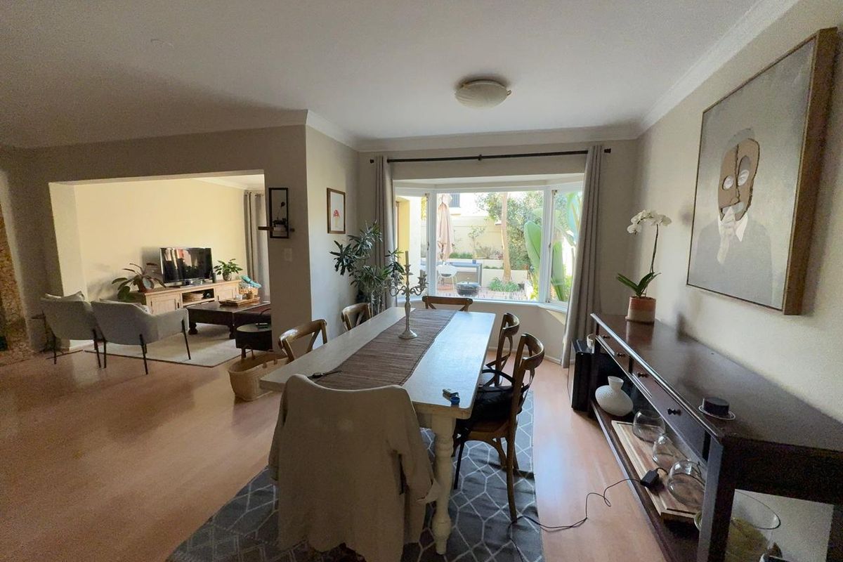 Spacious open-plan dining and living area featuring laminate flooring, a large bay window, and seamless flow to the outdoor patio space.