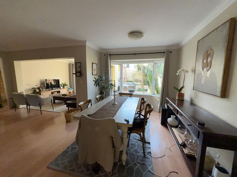 Spacious open-plan dining and living area featuring laminate flooring, a large bay window, and seamless flow to the outdoor patio space.