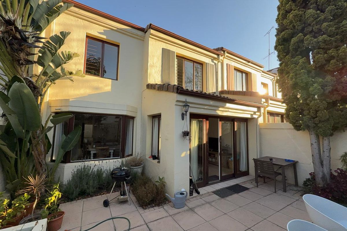 Rear view of the townhouse featuring a paved patio area, sliding glass doors, and established garden elements.